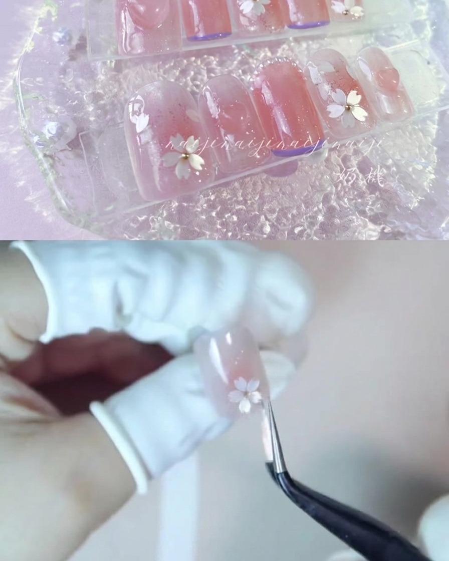 Unas pinzas colocando cuidadosamente fragmentos de pétalos de flores de cerezo blancos sobre una uña brillante.