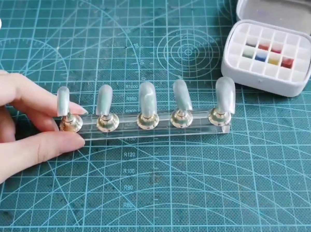 Un pincel plano para uñas tomando pigmento azul y morado de una paleta de gel de múltiples pozos.