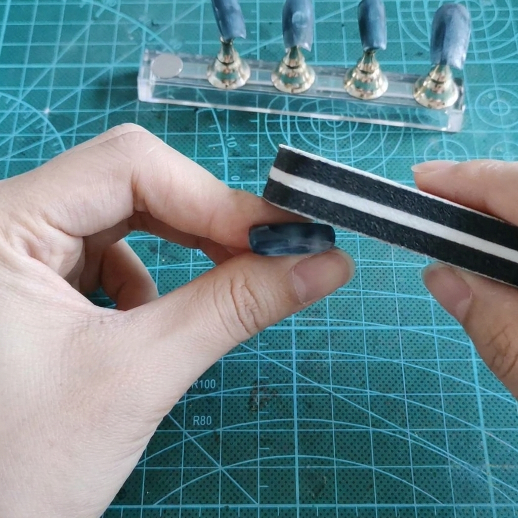 Una esponja pulidora lijando la superficie de gel brillante de una uña postiza sostenida entre los dedos.