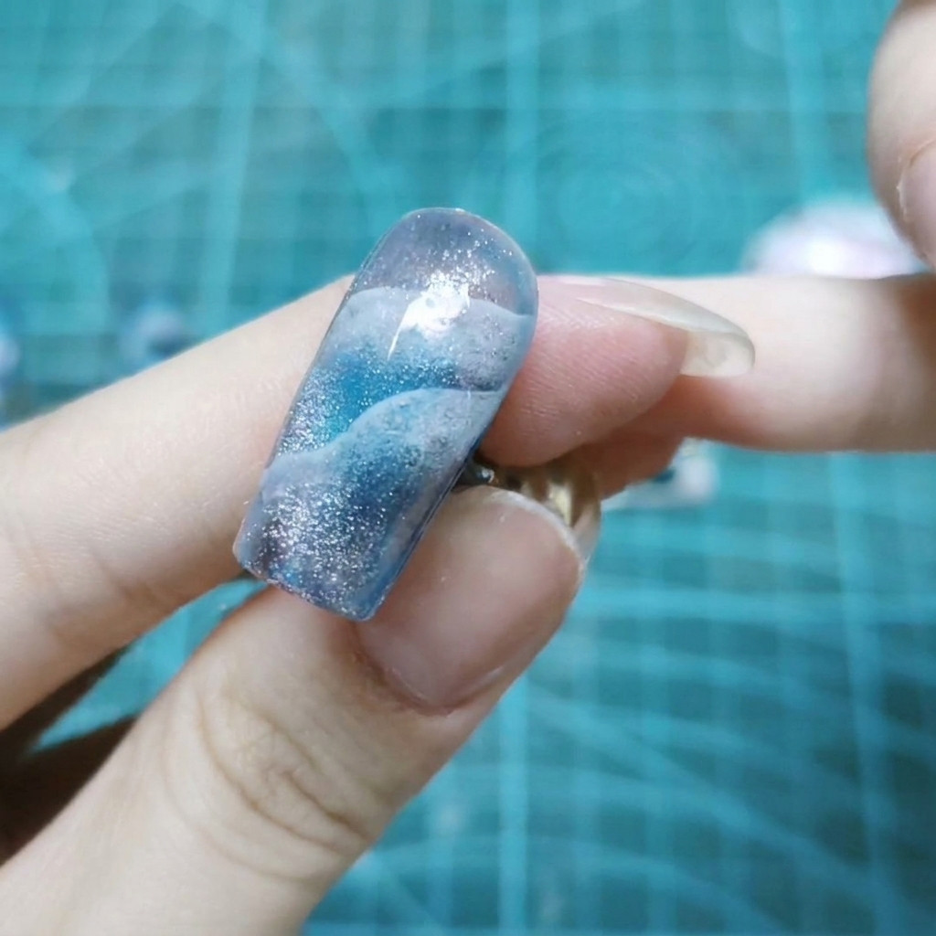 Una vista de cerca de una sola uña cubierta con purpurinas holográficas brillantes incrustadas en gel transparente.