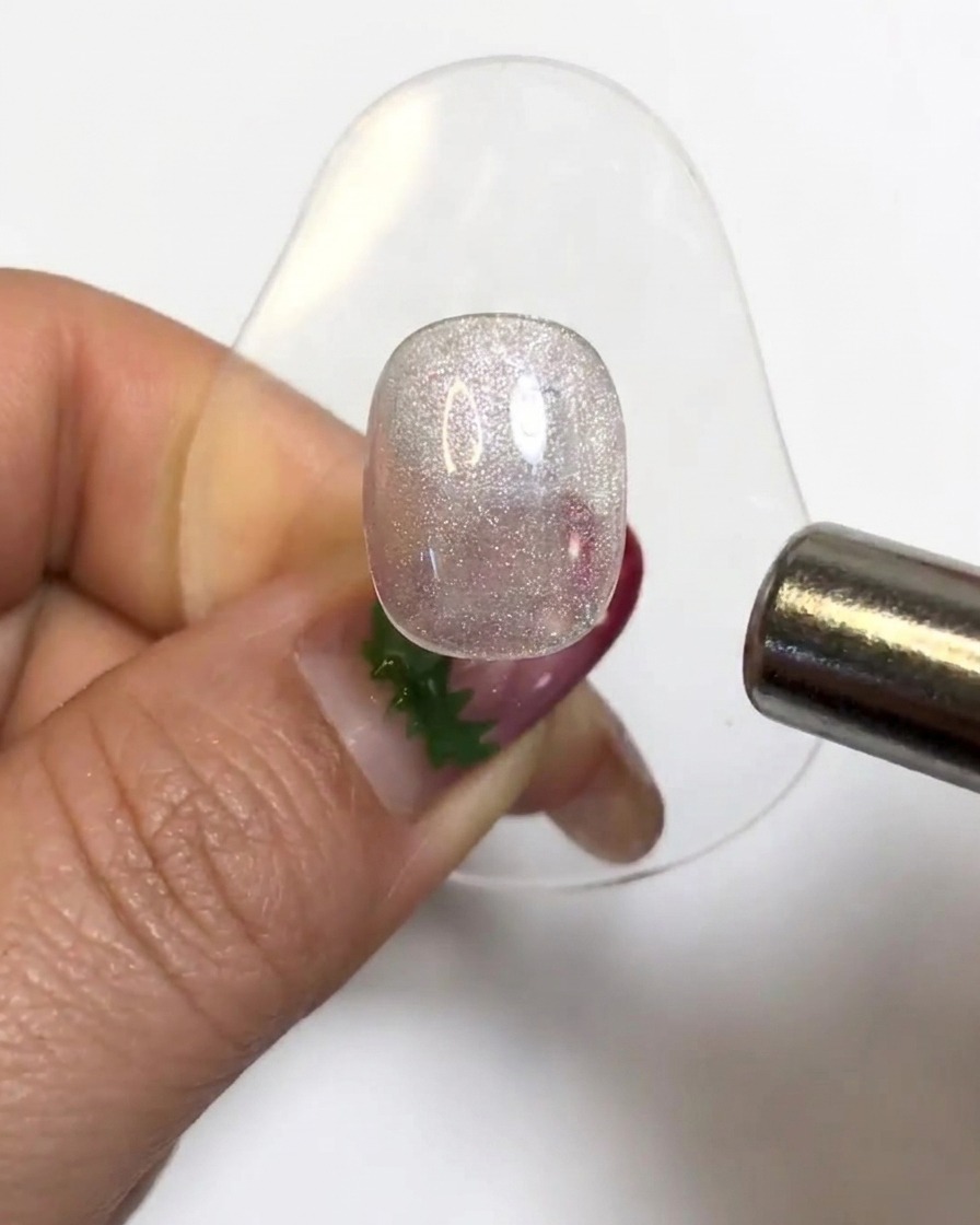 Un imán cilíndrico flotando sobre un tip de uña de gel brillante para activar las partículas del ojo de gato.