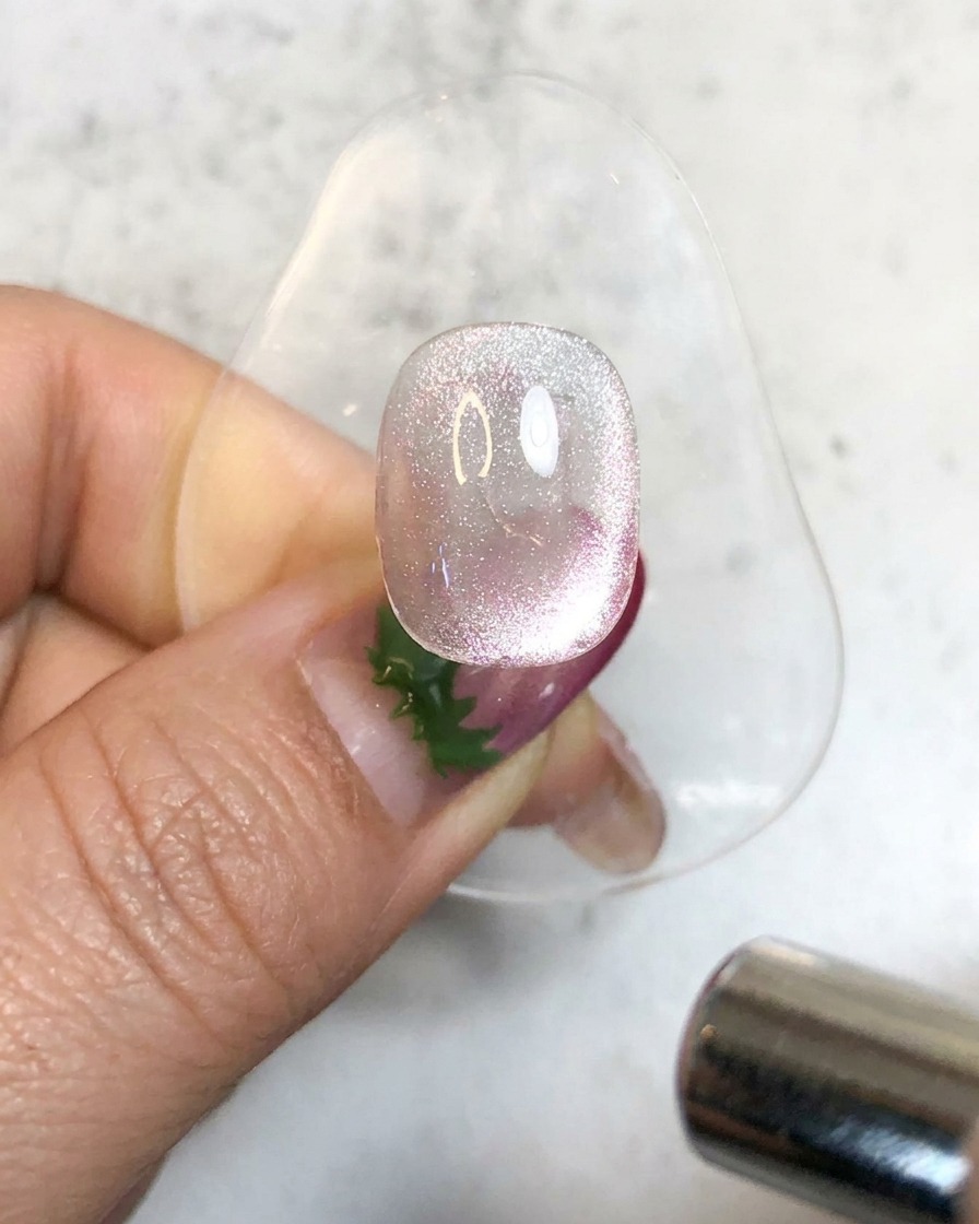 Una lámpara UV de mano iluminando una uña de gel magnética brillante en un soporte para curarla.