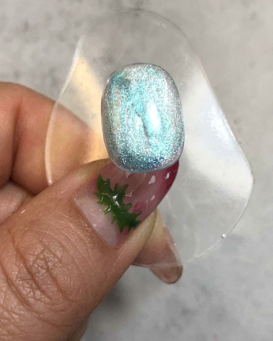 Una uña colocada dentro de una lámpara de curado con una luz brillante emitida alrededor de la superficie de gel azul translúcido.