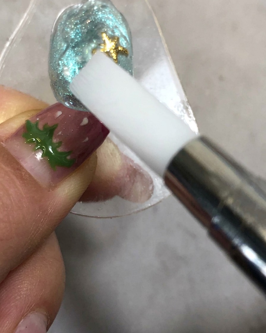 Una mano sosteniendo una herramienta de modelado de silicona cerca de una uña bajo una lámpara de curado.