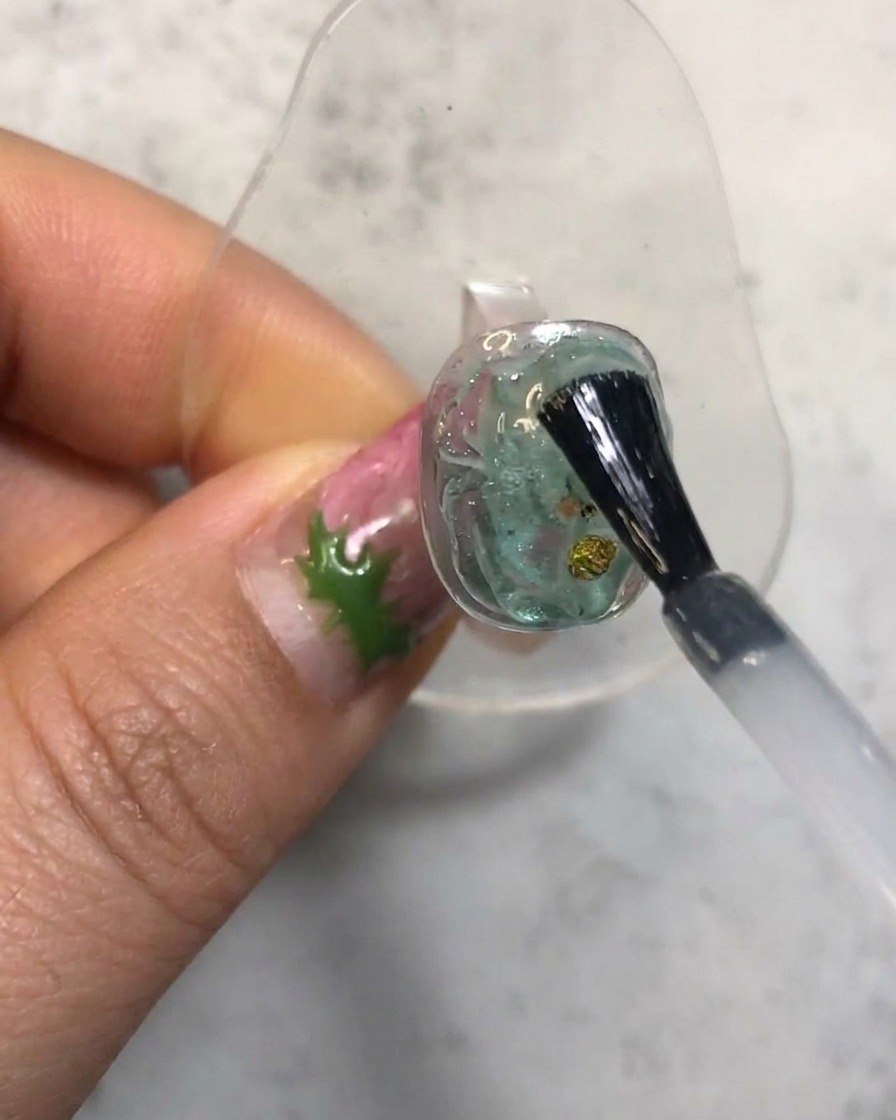 Un pincel de uñas aplicando un top coat transparente sobre una uña de gel translúcido texturizado.