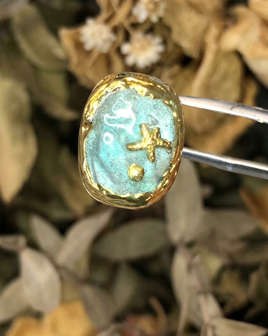 Unas pinzas sosteniendo una pieza de arte de uñas temática Atlantis terminada con marco dorado.