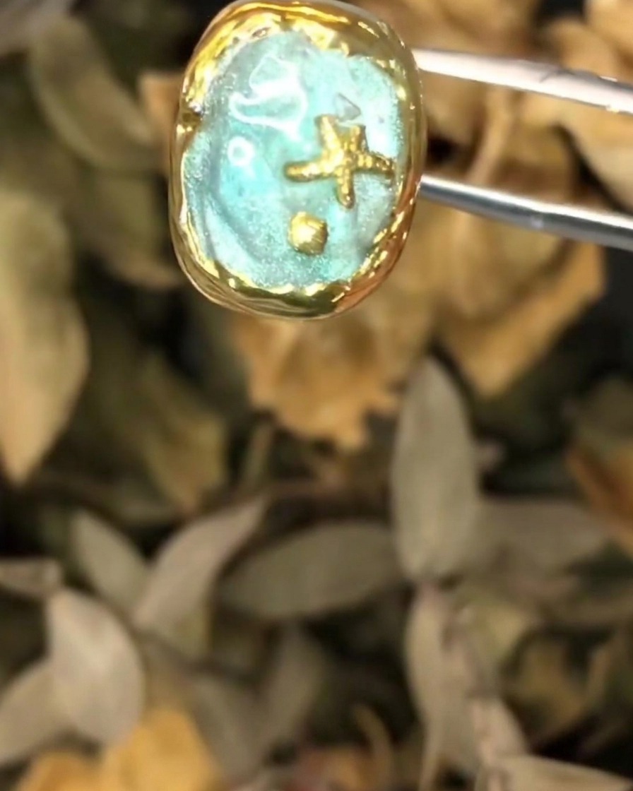 Unas pinzas sosteniendo la pieza de arte de uñas oceánicas texturizada durante la aplicación de la capa final.