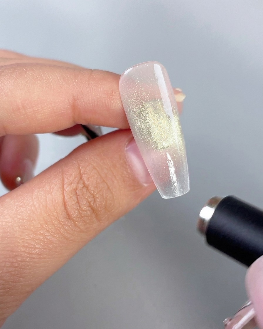 Una varita magnética cilíndrica sostenida cerca de una uña de gel verde brillante para activar el efecto ojo de gato.