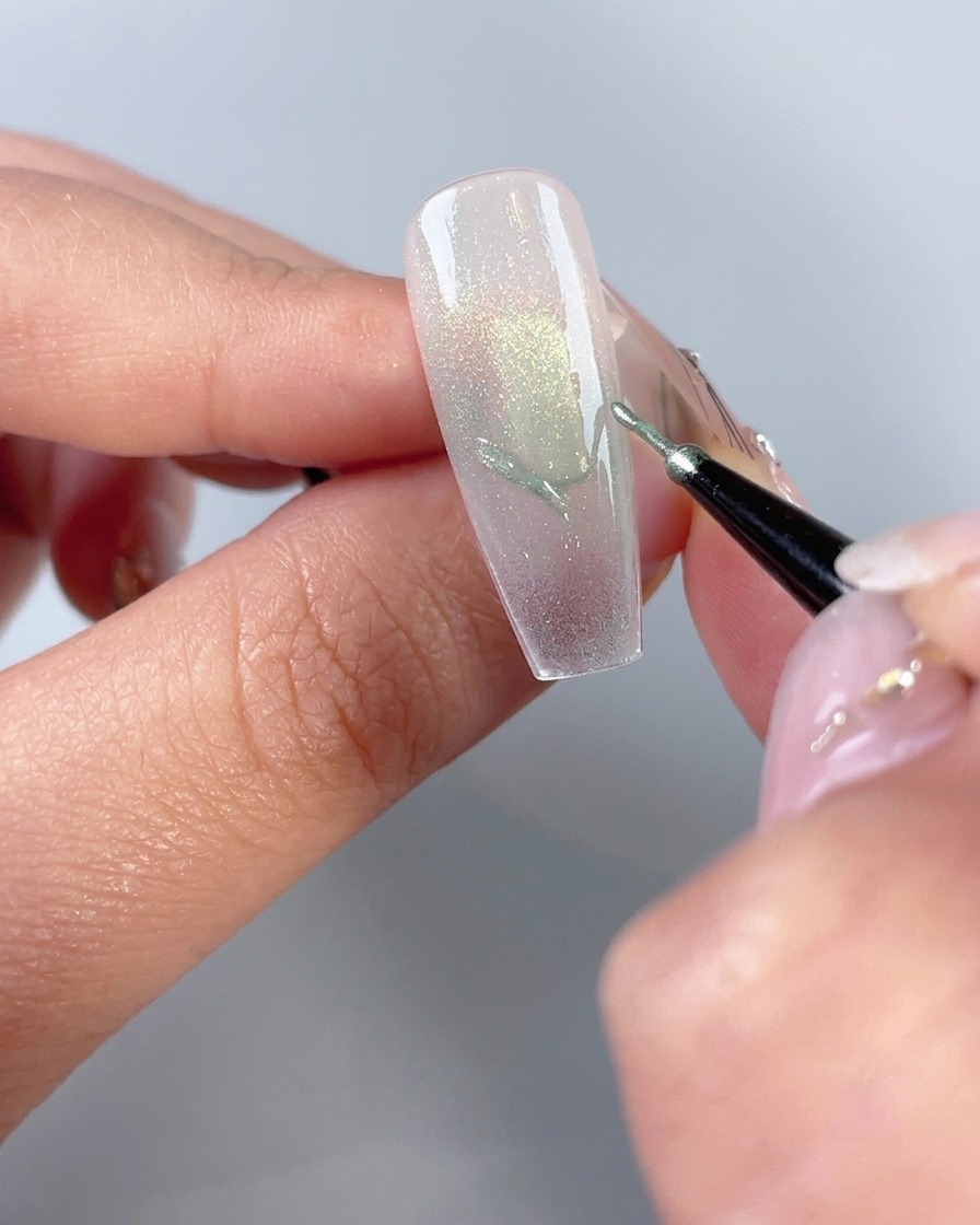 Un pincel fino de nail art dibujando los contornos de las alas de una mariposa en la punta de una uña arreglada.