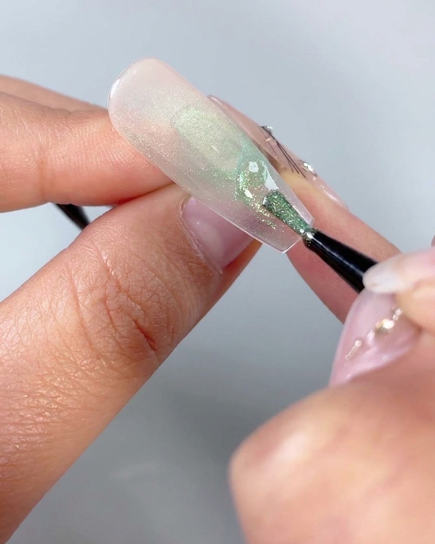 Un pincel fino de nail art dibujando pequeñas formas triangulares curvas cerca de la base inferior de un diseño de uña de mariposa.