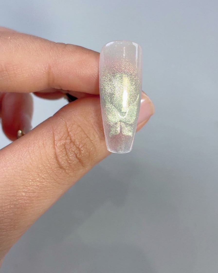 Un primer plano de una punta de uña transparente que muestra formas brillantes de alas de mariposa de ojo de gato verde después de la activación magnética.