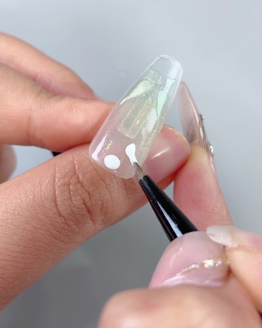Un pincel de arte fino aplicando puntos de gel blanco y trazos iniciales cerca del área de la cutícula de una uña.