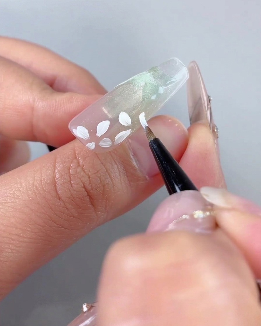Un pincel de arte fino agregando detalles de pétalos blancos más pequeños alrededor de la base floral grande pintada previamente.