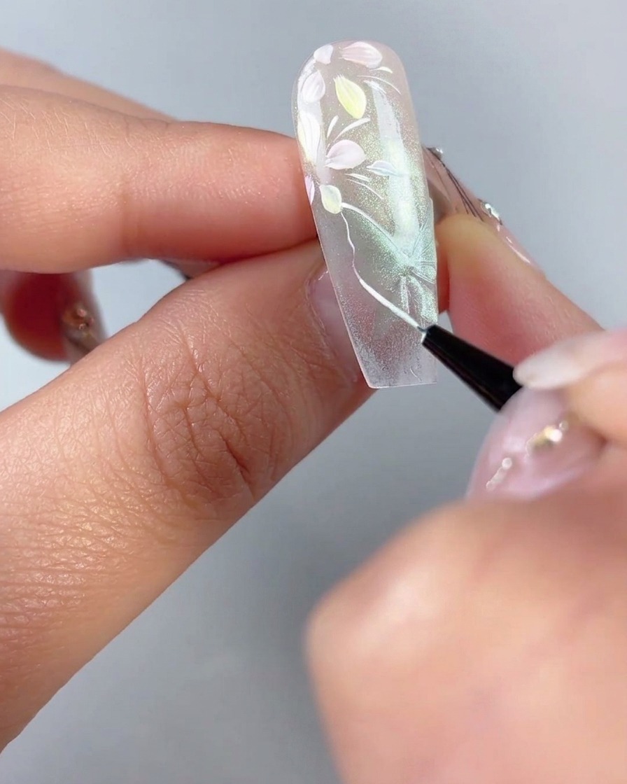 Un pincel delineador fino que traza contornos blancos finos y venas de las alas sobre una forma de mariposa de ojo de gato verde transparente en una uña.