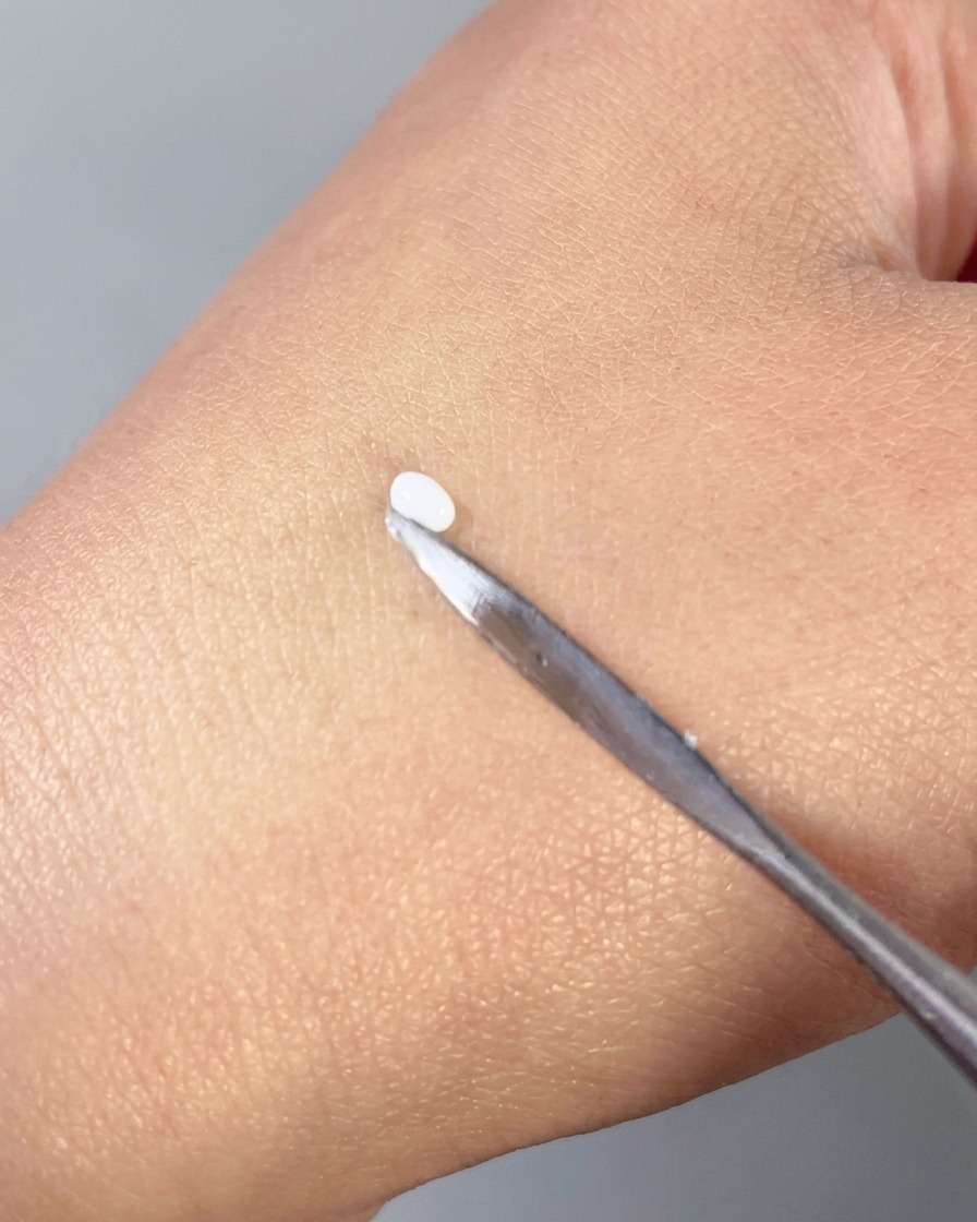 Una espátula de metal presionando una pequeña gota de gel blanco 3D en una forma de pétalo suave en el dorso de una mano.