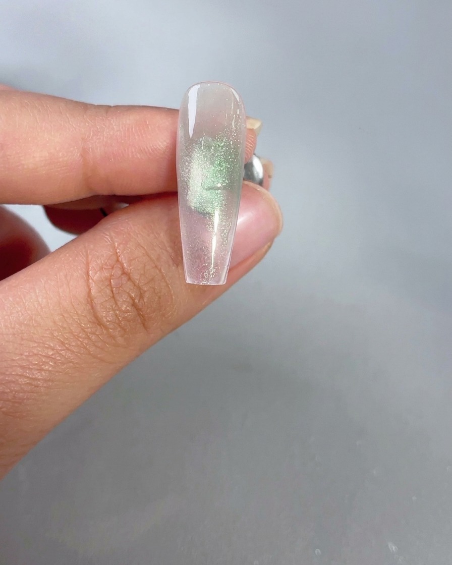 Un imán sostenido cerca de una uña de gel de ojo de gato verde translúcido para activar el efecto de brillo.