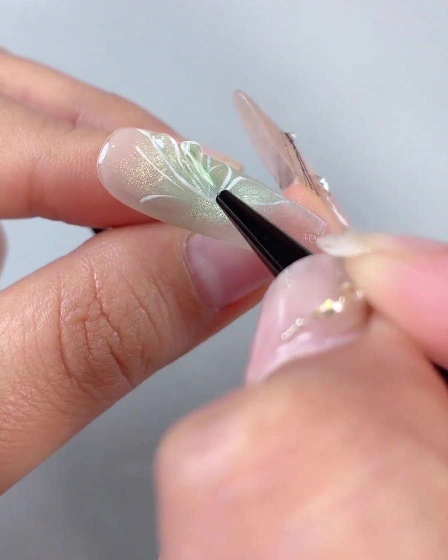 Un pincel delineador fino aplicando gel de modelado 3D transparente sobre los contornos de las alas pintadas de blanco de un diseño de uña de media mariposa.
