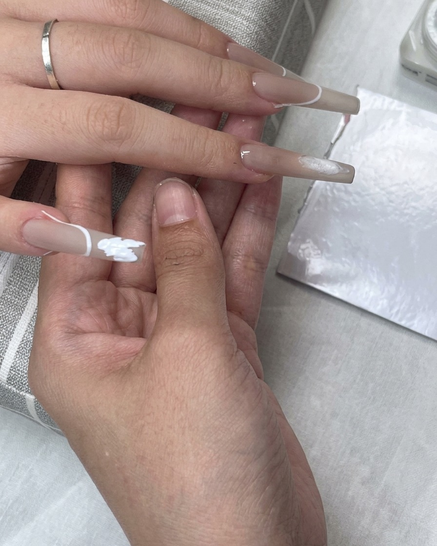 Una pegatina guía para punta francesa colocada en la uña mientras el esmalte de gel blanco rellena la zona de la punta.