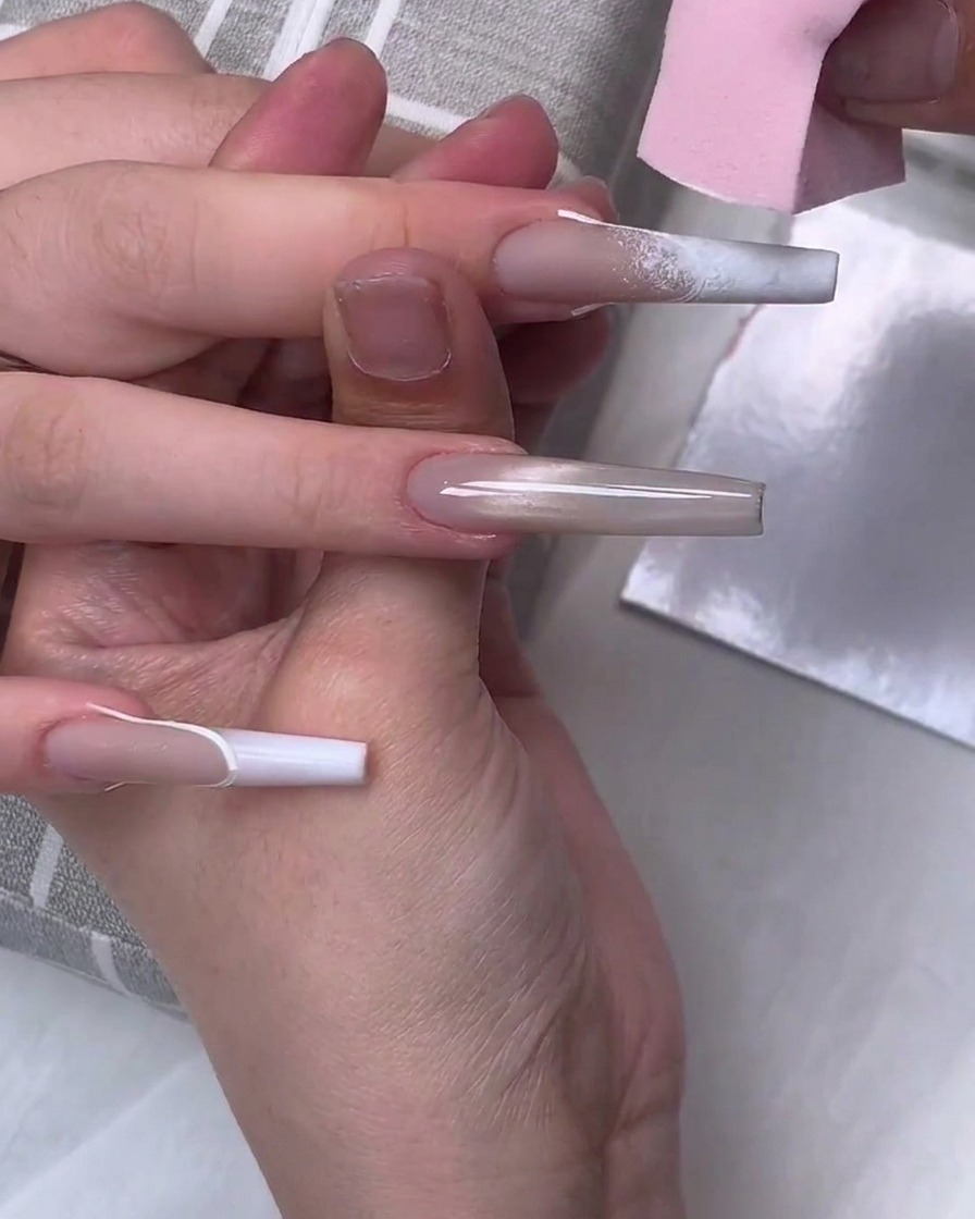 Una esponja de maquillaje rosa aplicando esmalte de gel blanco en la punta de una uña larga en forma de ataúd para crear un efecto degradado.