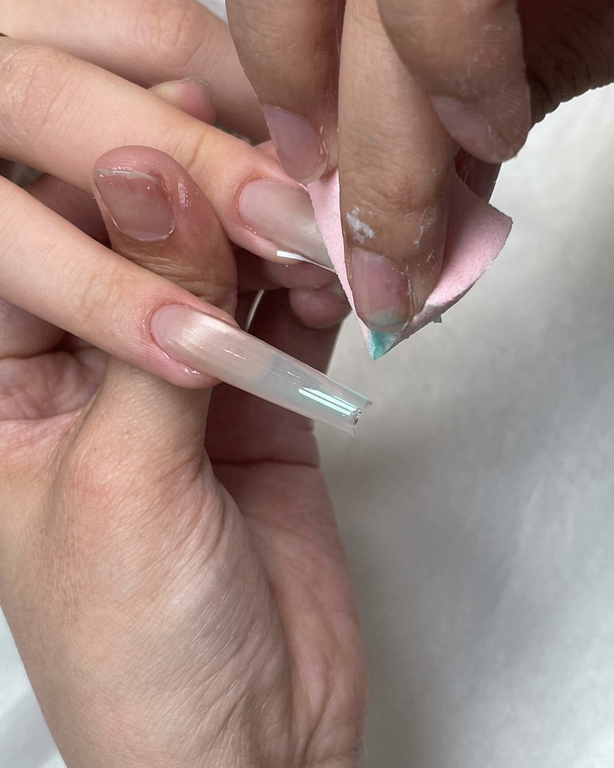 Una esponja de maquillaje rosa difuminando puntos de gel azul sobre la punta francesa blanca de una uña larga.