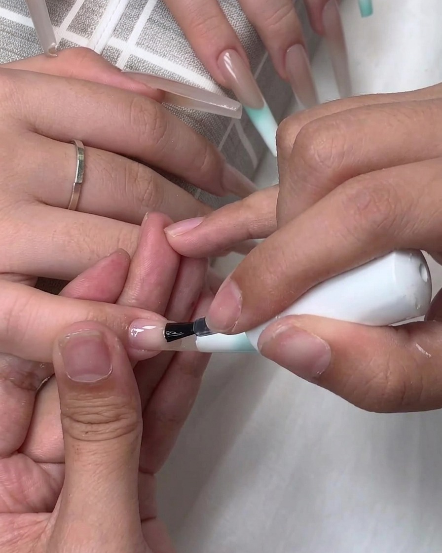 Un pincel aplicando una capa base transparente o top coat sobre la superficie de una uña postiza.