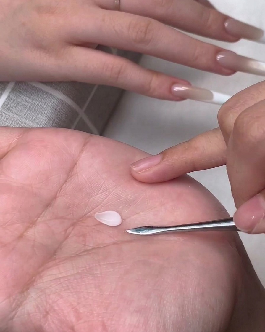 Un pequeño pétalo de gel 3D blanco en forma de lágrima sobre la palma de una persona junto a una herramienta de metal para esculpir.