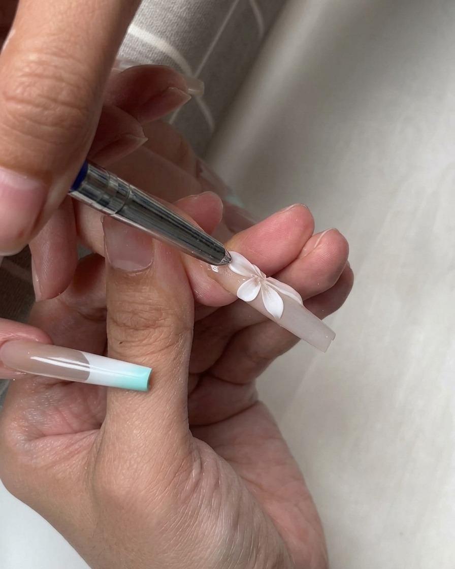 Una herramienta de silicona dando forma a múltiples pétalos blancos en 3D dispuestos en una flor completa sobre una uña.