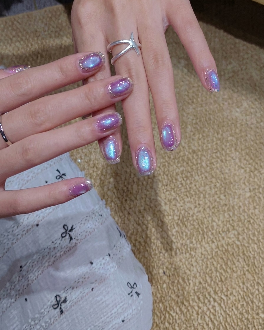 Un pincel aplicando una capa de esmalte de gel ojo de gato azul y morado brillante sobre una uña.