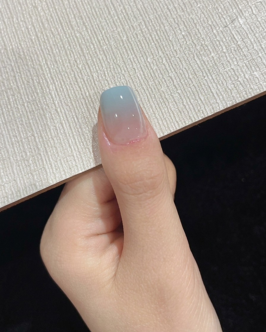 Un pulgar posicionado bajo una lámpara portátil UV LED durante el paso final de curado del top coat.