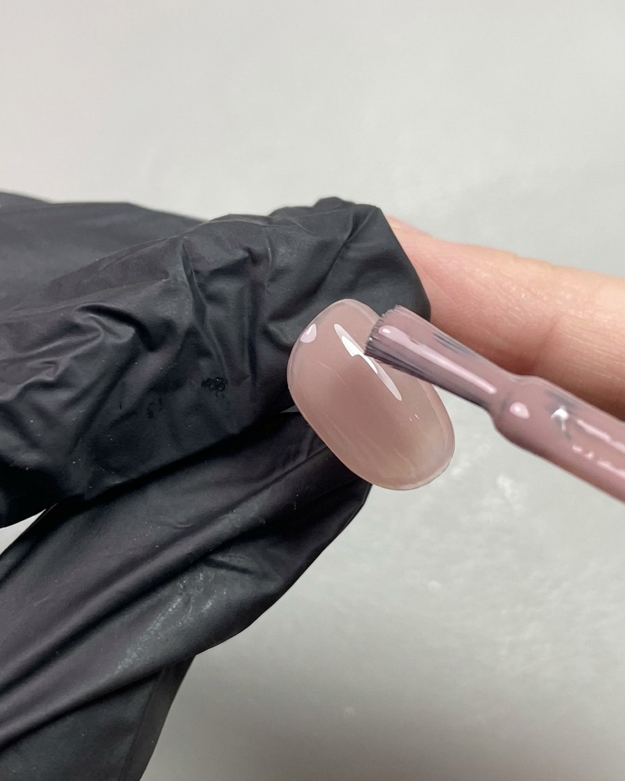 Un pincel aplicando una segunda capa de gel traslúcido en tono nude anaranjado sobre una uña.