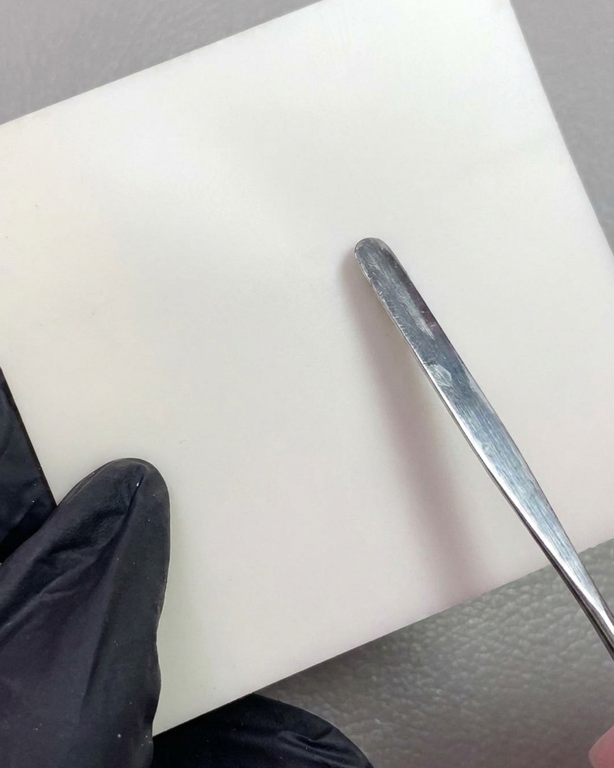 Una herramienta metálica colocando una porción de gel de modelado blanco sobre un papel de mezcla blanco y limpio.