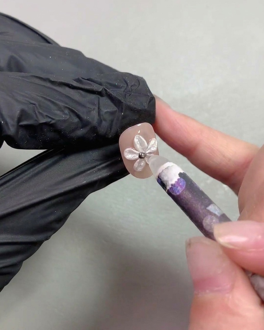 Una herramienta de lápiz de cera colocando diminutas cuentas de acero metálico en el centro del nail art con flor de perlas.