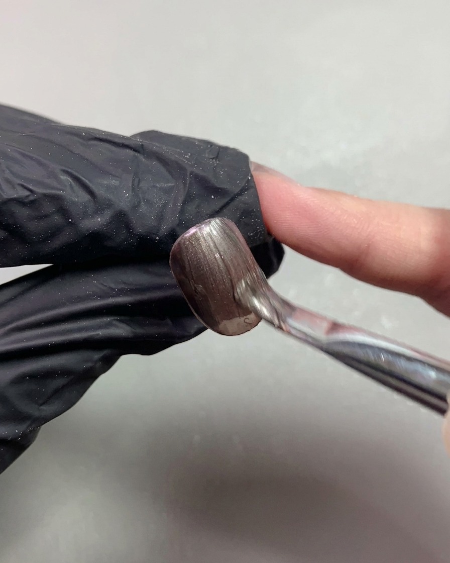 Un pincel aplicando gel magnético de ojo de gato marrón oscuro suavemente sobre una uña corta.
