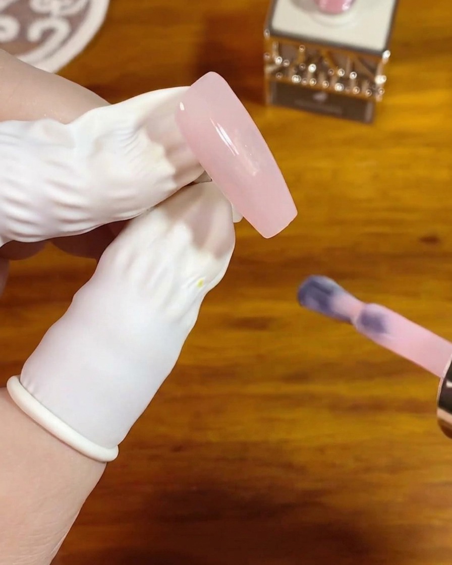Un pincel para uñas aplicando una capa suave de gel cristal rosa translúcido sobre una uña larga y cuadrada natural.