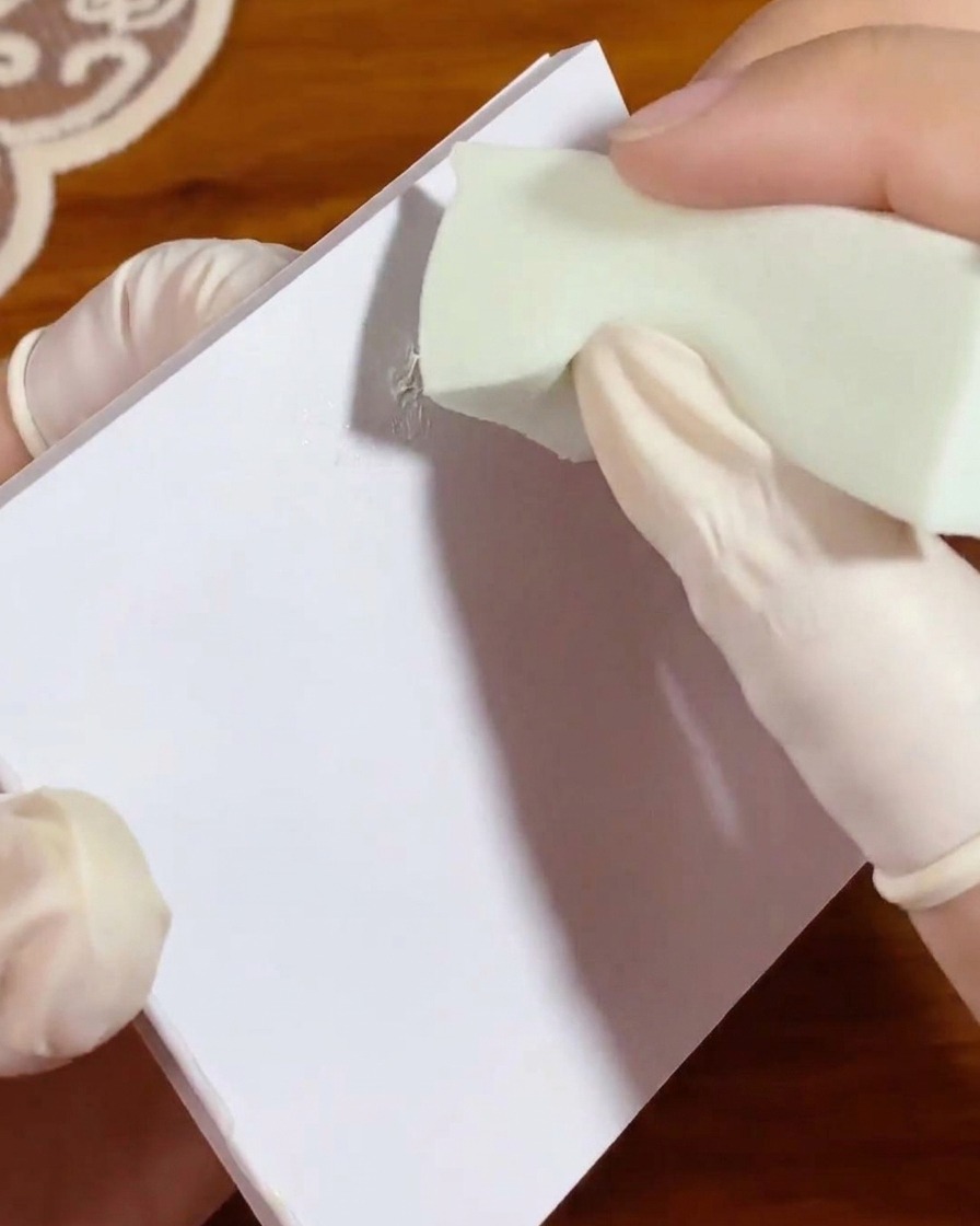 Una pequeña esponja de maquillaje verde dando toques en un área de gel blanco sobre una paleta para distribuir el color uniformemente.
