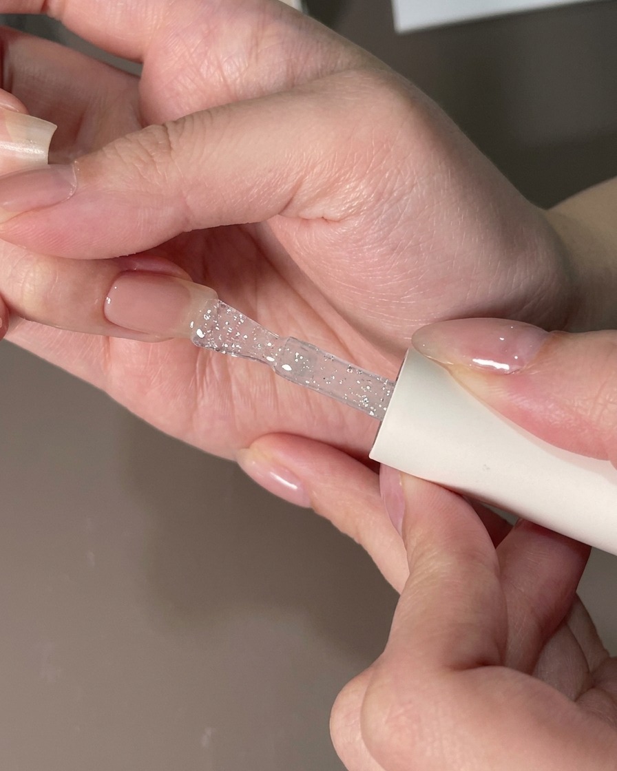 Un pincel plano alisando una capa de gel transparente sobre una uña para eliminar partículas.
