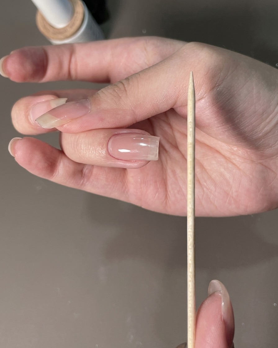 Una lima de uñas sostenida junto a una mano manicurada para dar forma a los bordes de la uña.