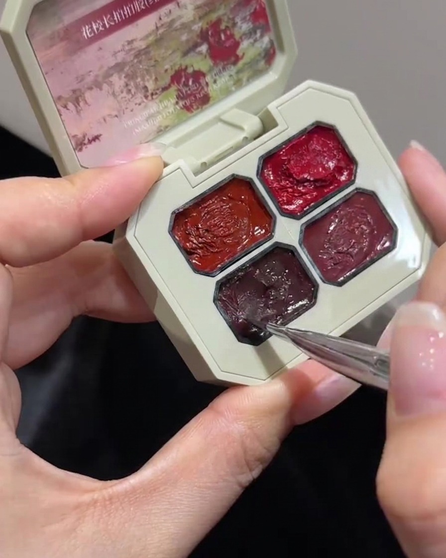 Un primer plano de un pincel fino de nail art sumergiéndose en un compartimento específico de una paleta de gel de toque de color rosa.