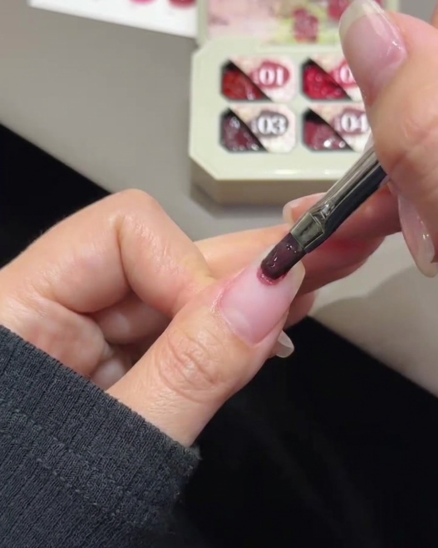 Un pincel de uñas aplicando gel rosa a toquecitos en la punta de una uña natural.