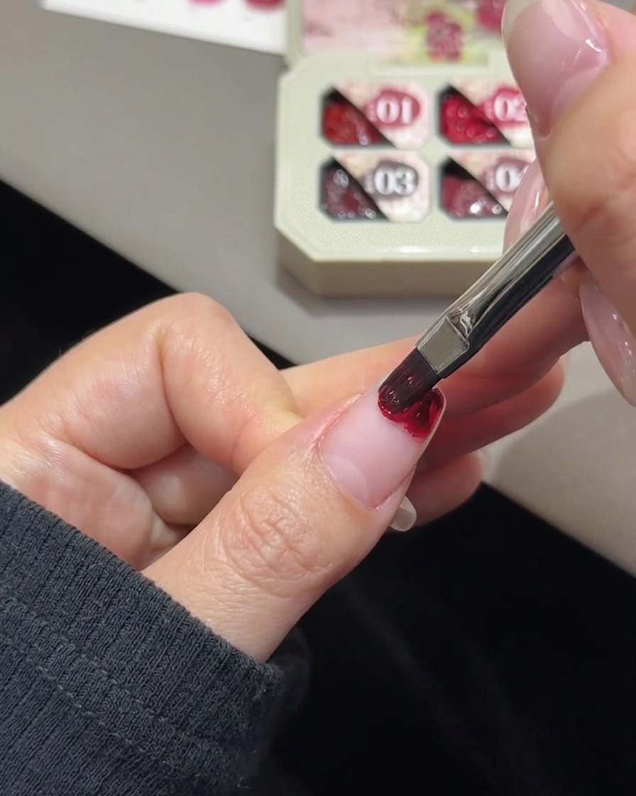Una pequeña esponja de maquillaje blanca en forma de cuña difuminando el color del gel rosa en la punta de una uña.