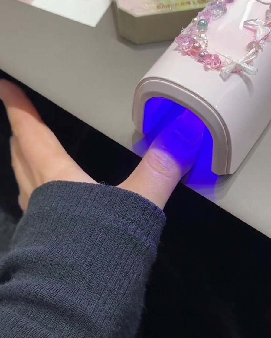 Una uña curándose bajo una lámpara UV/LED rosa.