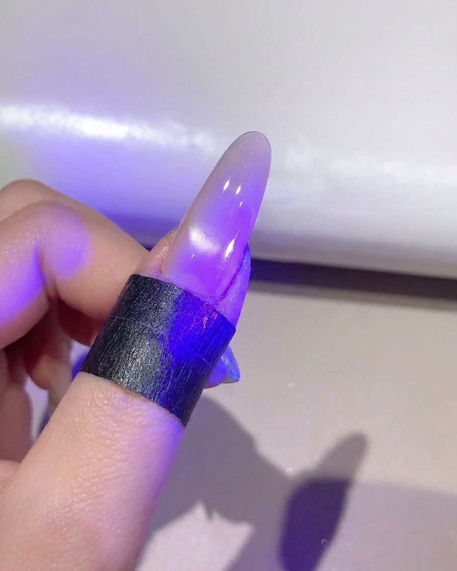Una uña bajo una lámpara UV/LED violeta curando la capa de gel ojo de gato terminada.