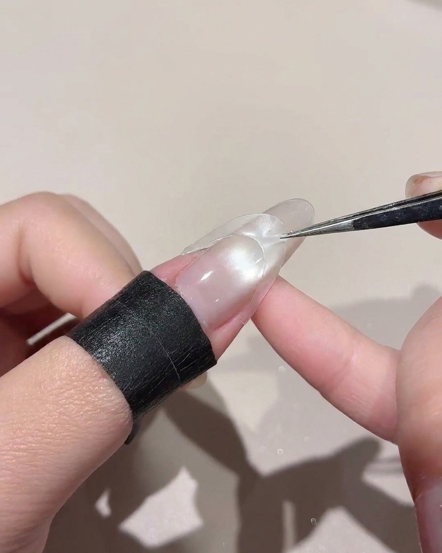 Una pegatina curvada siendo colocada a través del medio de una uña brillante usando pinzas.