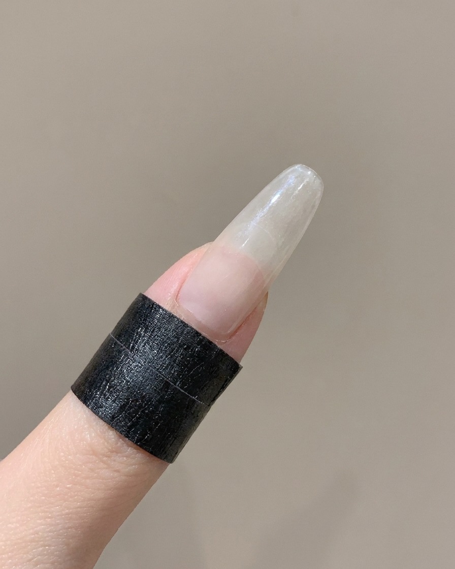 Una herramienta de silicona presionando el borde curvado de una pegatina para uñas francesa en un dedo.