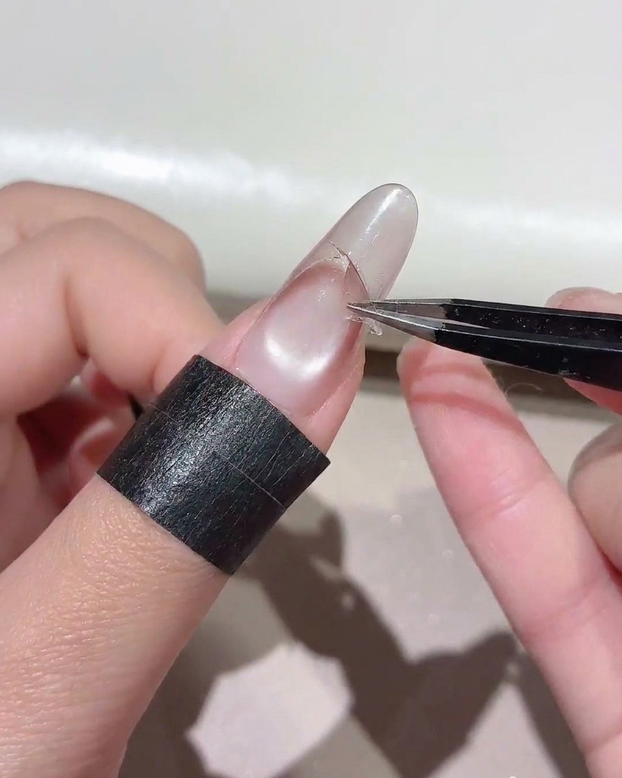 Pinzas tirando de una pegatina curvada de una uña para exponer una línea de degradado nítida.