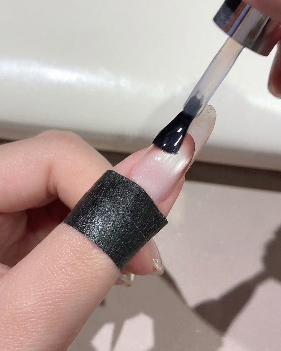 Un pincel aplicando top coat transparente a través de toda la superficie de una uña manicurada.
