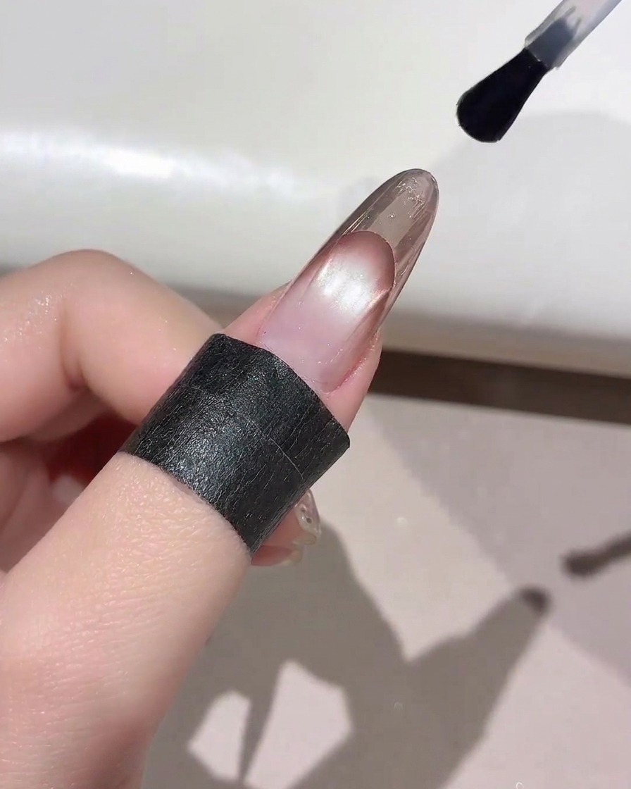 Un pincel de uñas aplicando un top coat transparente sobre la punta de una manicura francesa terminada.