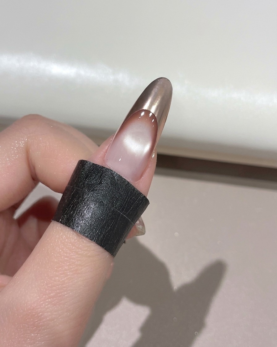 Un dedo con una punta francesa de cromo dorado descansando dentro de una lámpara de uñas UV para su curado.