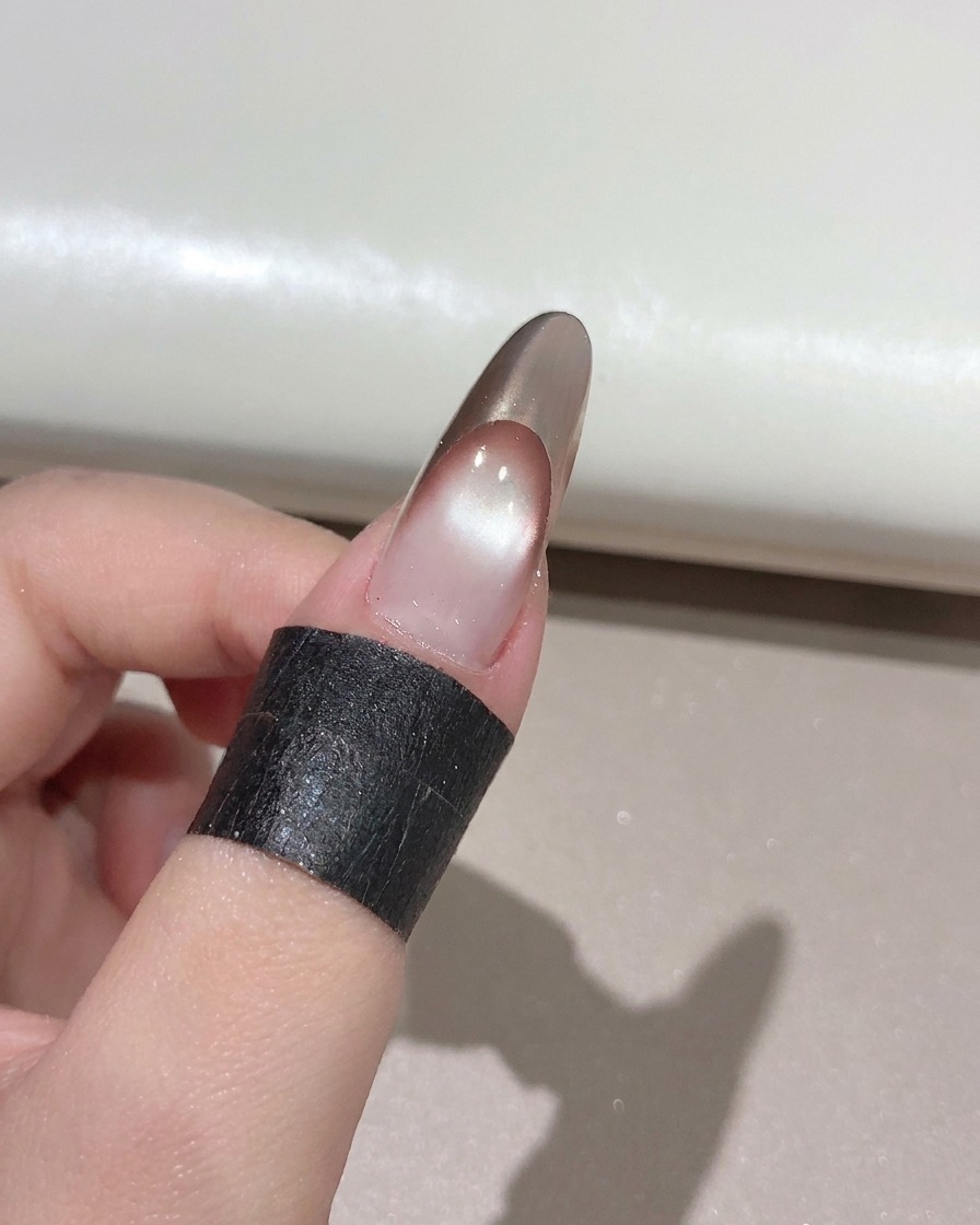 Un pincel de uñas aplicando un top coat brillante y transparente sobre una manicura francesa en oro rosa terminada.