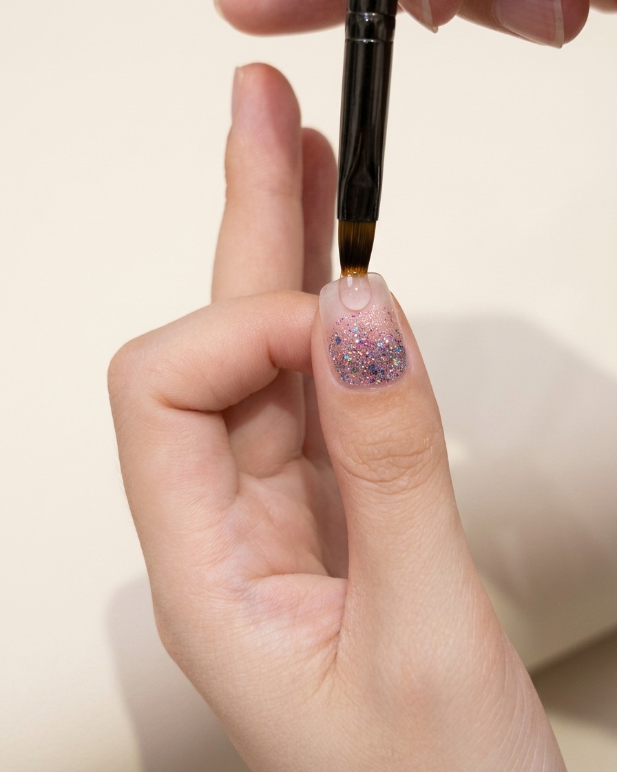 Primer plano de la uña del pulgar que muestra una capa de degradado de glitter inspeccionada bajo iluminación cálida.